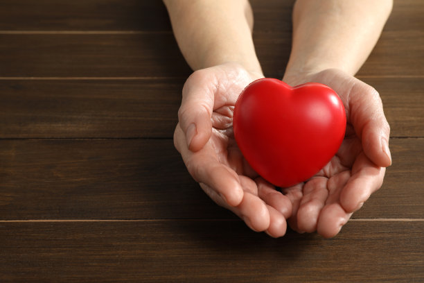 老年妇女手持红心在木桌，特写。文本空间图片下载