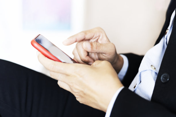 商人坐在沙发上用手机。侧视图的休闲男子使用模拟智能手机，而坐在沙发上在客厅。图片下载