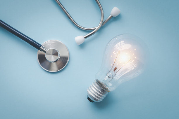 医生的听诊器，面朝下放在桌子上，用蓝色色调处理过。将心脏监护仪、听诊器和灯泡平铺在蓝色背景上。图片下载