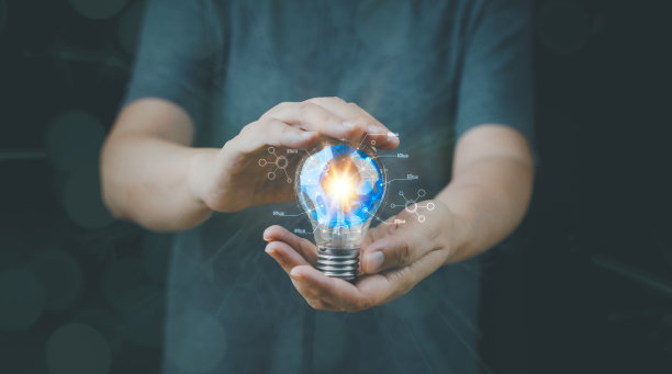 一个男人的手拿着一个灯泡，里面有一个蓝色的地球仪，他正在使用一台笔记本电脑。灵感来自网络技术。创新理念概念。图片下载