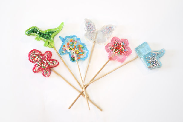 白色背景上的彩色棒棒糖。恐龙、独角兽、花朵和蝴蝶形状的漂亮棒棒糖图片下载