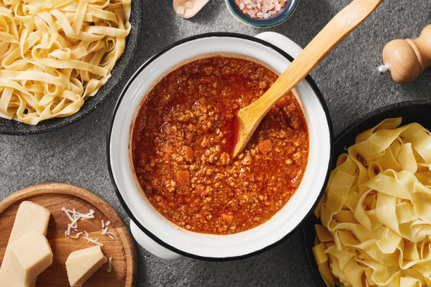 一锅新鲜的意大利肉酱和一锅煮熟的意大利宽面条。灰色背景来自天然石材。前视图。图片下载