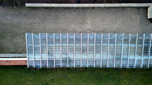 木制结构的凉棚由光滑的圆柱形白色圆柱支撑，是凉亭凉棚的遮蔽物。屋顶内衬玻璃。连接到带砖屋顶、草坪、鸟瞰图的挡土墙图片下载