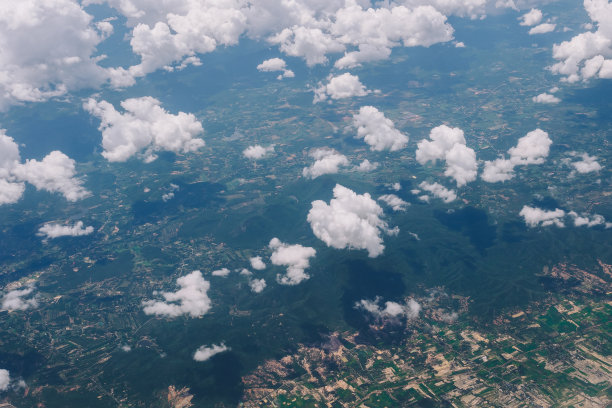 鸟瞰森林、山脉、草地和丰富的种植园，被白色蓬松的云覆盖图片下载