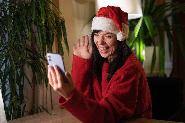 快乐的年轻女子在圣诞老人的帽子挥手使用智能手机应用程序享受在线虚拟聊天视频电话与朋友，虚拟圣诞会议。为社交媒体记录故事的博主图片下载