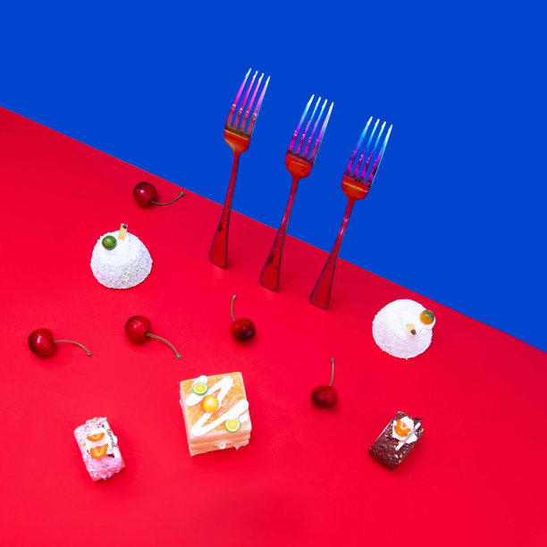 闪闪发光的叉子配上蓝色的壁纸，糖果和樱桃配上红色的背景。前视图。超现实的创意构图，未来派糕点店或餐厅的广告。图片下载