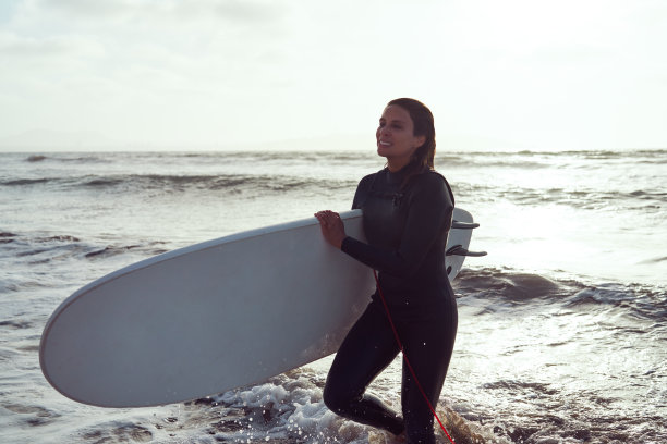 肖像中期成年拉丁女子冲浪者与冲浪板走出水面微笑图片下载