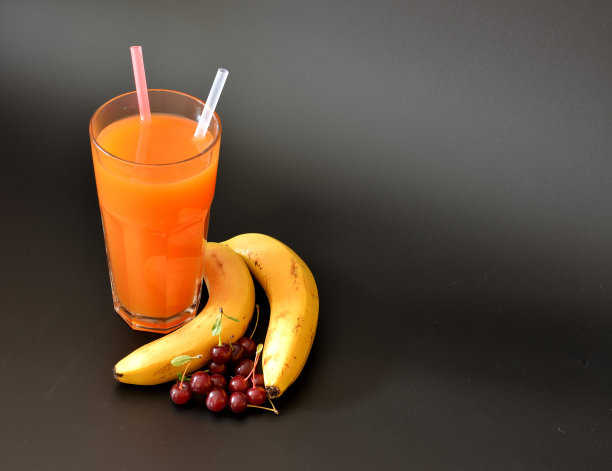 一大杯果汁，上面有稻草和成熟的樱桃，黑色背景上有一根香蕉。图片下载