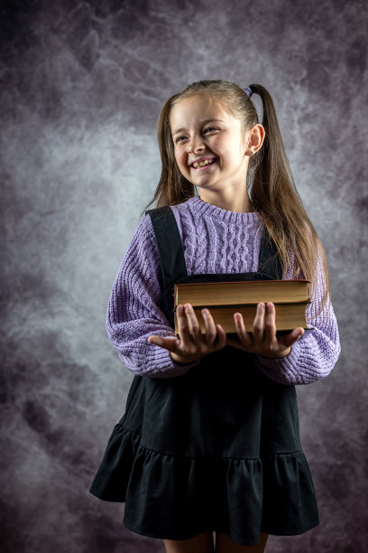 微笑着美丽的小女孩手里拿着厚厚的书，孤立在朴素的背景上。图片下载