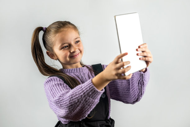 可爱的小女孩抱着平板电脑微笑孤立在朴素的背景。图片下载