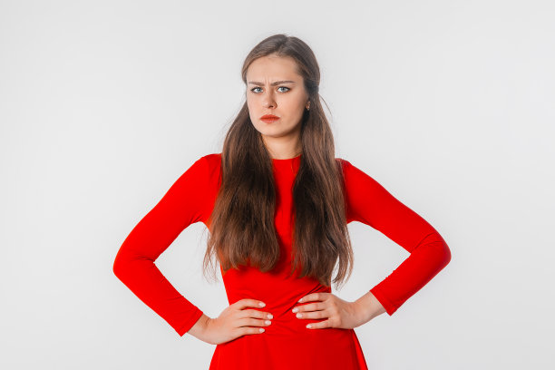 自信的年轻女商人在红色连衣裙手放在臀部，看着相机，站在白色的工作室背景图片下载