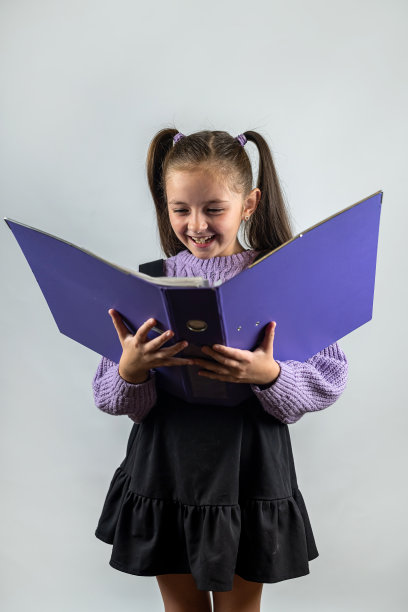 有趣的微笑的孩子女学生拿着书在她的手中。孤立的平原背景。图片下载