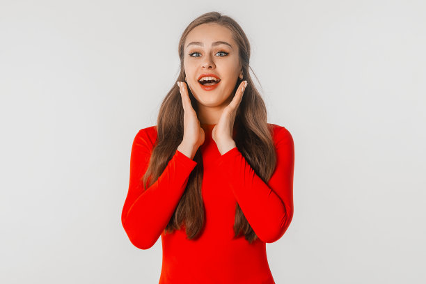 美丽的震惊和惊讶的女人张开了嘴。惊讶的女孩用手抱着脸颊，站在白色的工作室背景。漂亮女人表示非常惊讶图片下载