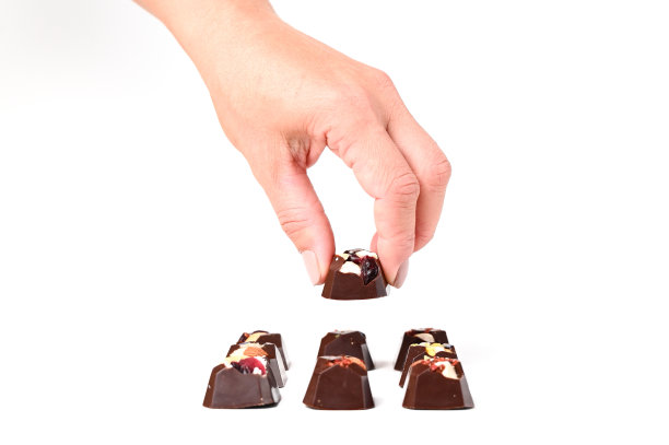 示范的巧克力糖果与坚果或水果馅，女性手与美甲握住甜，白色表面图片下载