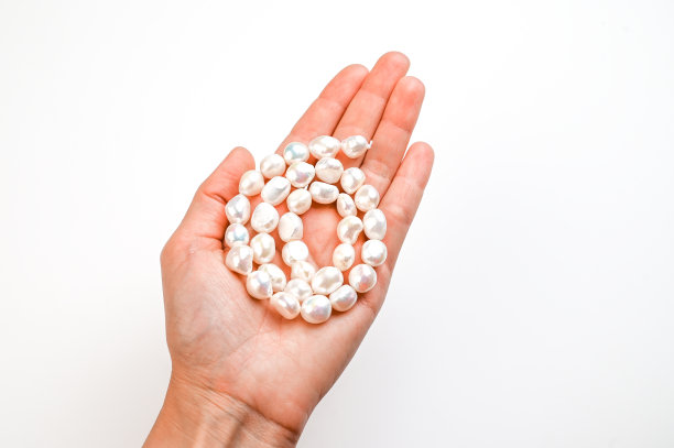 特写的女人手与白色巴洛克珍珠串孤立在白色。短发手握珍珠图片下载