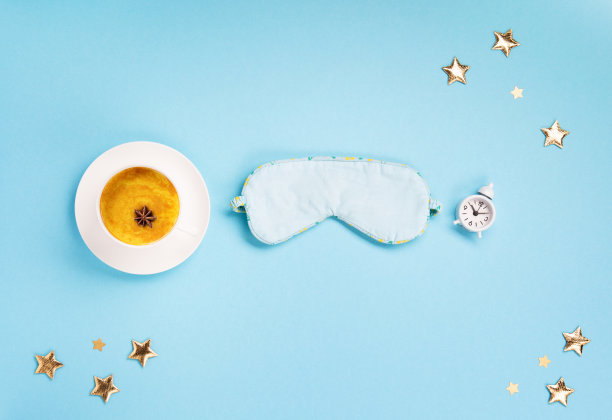 睡眠面具，姜黄金色牛奶拿铁和闹钟在蓝色背景。世界睡眠日概念。图片下载