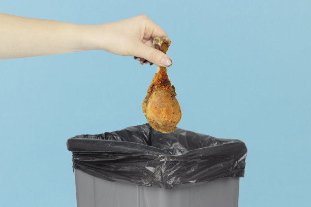 把鸡腿扔在垃圾桶里，鸡腿拿在手里放在垃圾桶前，素食主义的概念图片下载