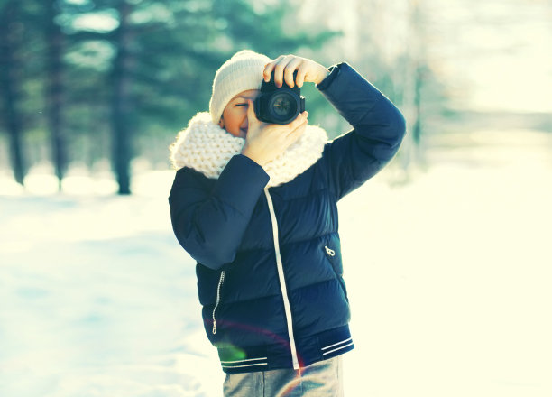 小男孩摄影师与相机拍摄森林景观在雪冬季公园图片下载
