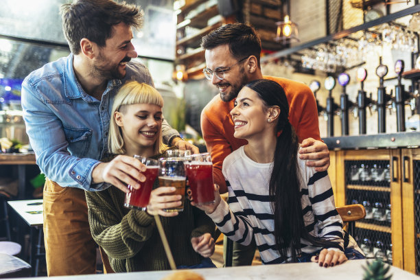 微笑的年轻朋友在酒吧喝精酿啤酒图片下载