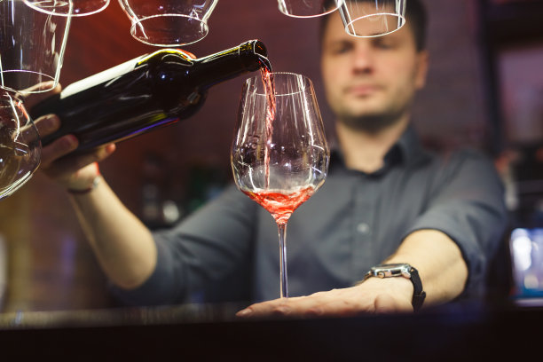 在昏暗的酒吧里，一名男子将红酒倒进玻璃杯图片下载