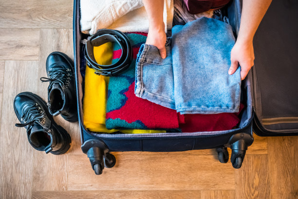 一个女人把她的衣服装进家里客厅的行李箱里。从上面看。旅行的概念。假期准备。图片下载