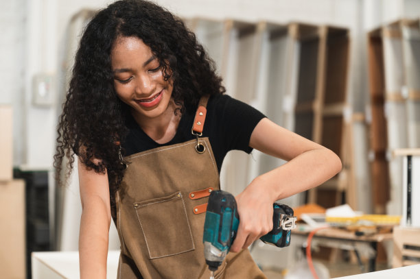 木工混合种族妇女使用电动螺丝刀在木材厂图片下载