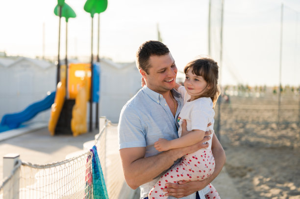 在落日的沙滩上，父亲和女儿一起在操场上玩耍。夏季户外活动的概念。图片下载