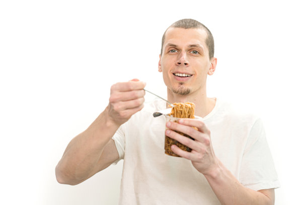 微笑的男人拿着叉子，白色背景的透明塑料杯里装着快餐面条。幸福。意大利面。吃东西。顿饭。饿了。食物。即时。快乐。小吃。兴奋。表达式图片下载