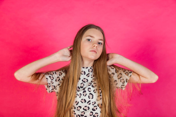 十几可爱的女孩的肖像长头发在休闲t恤站在粉红色的背景，看着相机摆姿势。漂亮的时尚少女金发女孩。时尚风格概念。本空间图片下载