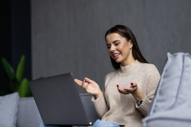 年轻快乐的女人有视频通话，坐在床上挥手对着笔记本电脑和微笑。图片下载