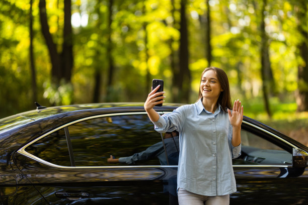 有问题的时间。年轻女子站在白色汽车背景下自拍的照片。图片下载