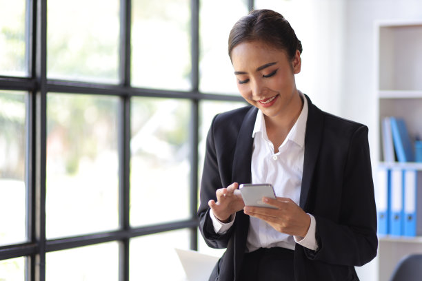 迷人的亚洲女商人在办公室检查智能手机上的工作时间表。图片下载