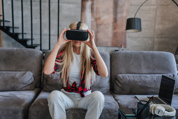 年轻美丽的瑞典女子在格子衬衫和白裤子使用vr眼镜回家。放松瑞典女孩在虚拟现实耳机坐在沙发上，楼梯上，玩游戏。休闲、游戏、网络空间。图片下载