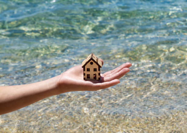 男孩小心翼翼地把房子模型举在清澈的海水上。孩子手中的房子和夏天的海滩。家庭度假物业，度假村，度假地产，拯救自然为家图片下载
