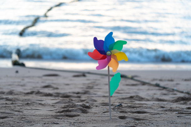 可爱的彩虹色的塑料风车在沙滩上日落与海浪的背景图片下载