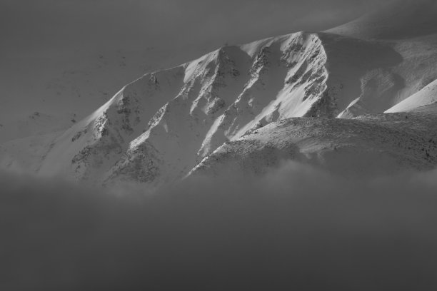 引人注目的冬季山地景观。白雪覆盖的朦胧的山峰和山丘。黑白照片。自然概念背景。图片下载