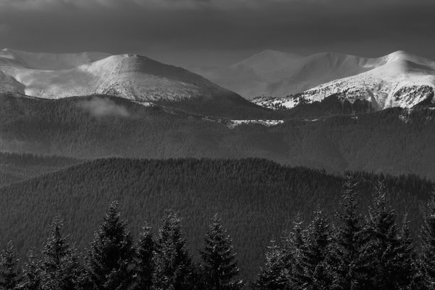 引人注目的冬季山地景观。白雪覆盖的朦胧的山峰和山丘。黑白照片。自然概念背景。图片下载
