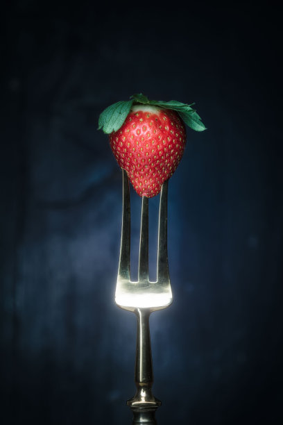 垂直拍摄的红色成熟草莓放在闪亮的不锈钢叉子上，与黑暗背景隔离开来图片下载