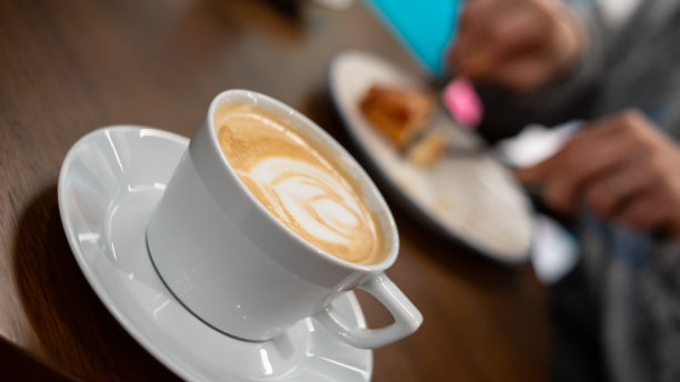 拿铁是在白色的杯子关注前景的妇女在背景是吃水平照片图片下载