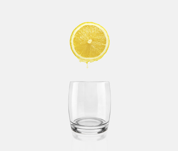 新鲜柠檬片滴在空玻璃杯上。保健概念图片下载