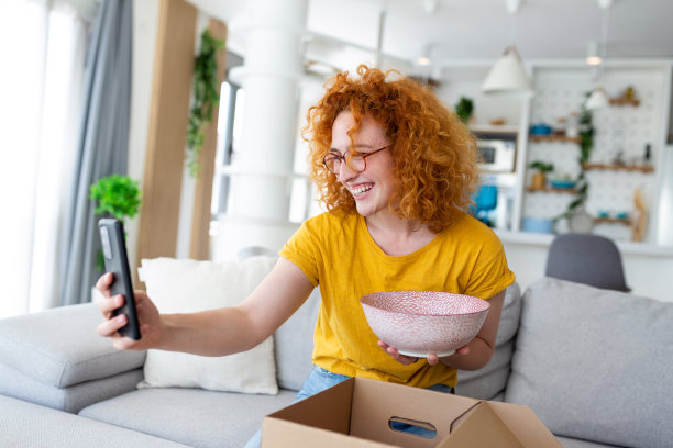 年轻满意的快乐女人购物狂客户坐在沙发上拆包裹快递箱，网购出货概念。拍摄产品照片并发布在社交媒体上图片下载