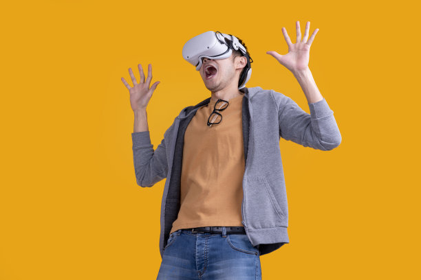 兴奋的亚洲成年男性戴着耳机vr虚拟护目镜小工具在运动休闲布玩体育在线游戏与有趣和快乐的面部表情在黄色背景工作室拍摄图片下载