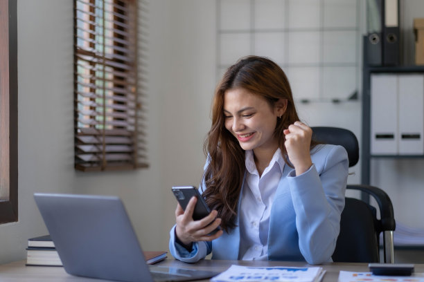 一个兴奋的年轻的亚洲女孩使用笔记本电脑和庆祝网上成功的肖像。图片下载