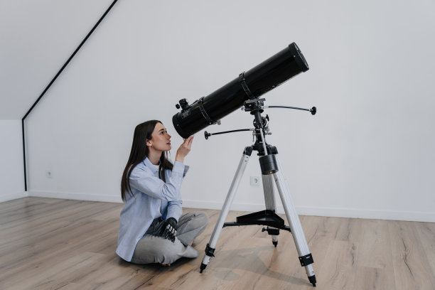 迷人的黑发白人女孩在休闲坐在地板上在家里用望远镜梦幻地仰望触摸手由人工仿生手臂假肢。创伤后康复。嗨技术。图片下载