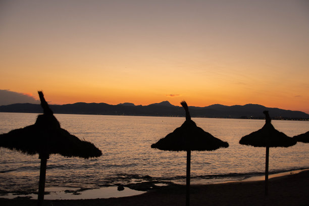 落日时分海滩上前景中的3把雨伞图片下载