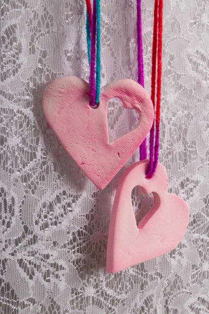 白色蕾丝窗帘前挂着两件粉色心形陶制装饰品图片下载