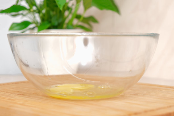 一名男子在透明玻璃碗的边缘打碎了一个鸡蛋。在家做饭的过程。炒鸡蛋，煎蛋卷，糕点，肉排，做早餐的原料。图片下载