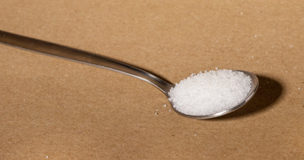 用勺子填满甜菜糖，白色甜味剂晶体。金属茶匙的甜味颗粒，粉末图片下载
