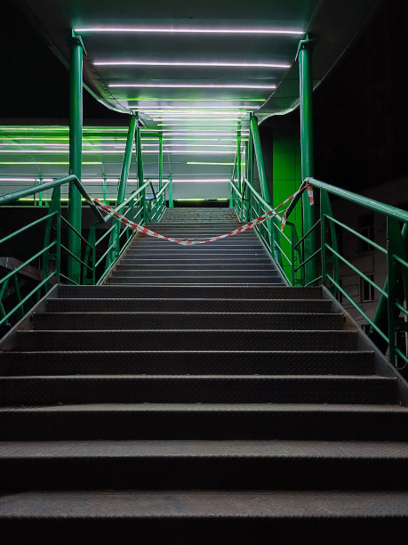 人行桥上有铁栏杆的夜楼梯被绿色的灯笼照亮。入口被禁带堵住了图片下载