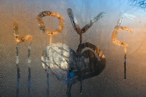 一颗画在模糊玻璃上的心。“爱”字写在湿玻璃上。爱与孤独的概念。图片下载